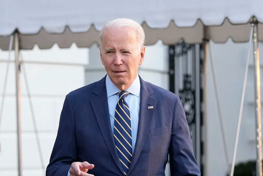 Joe Biden walking outside the White House, wearing a blue suit and a striped tie, with a serious expression.