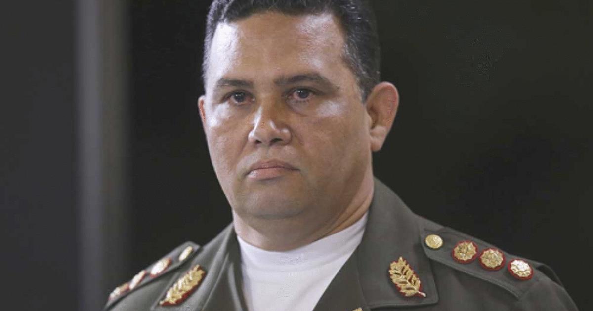 Portrait of a military officer in uniform, featuring insignia and medals, with a serious expression against a blurred background.