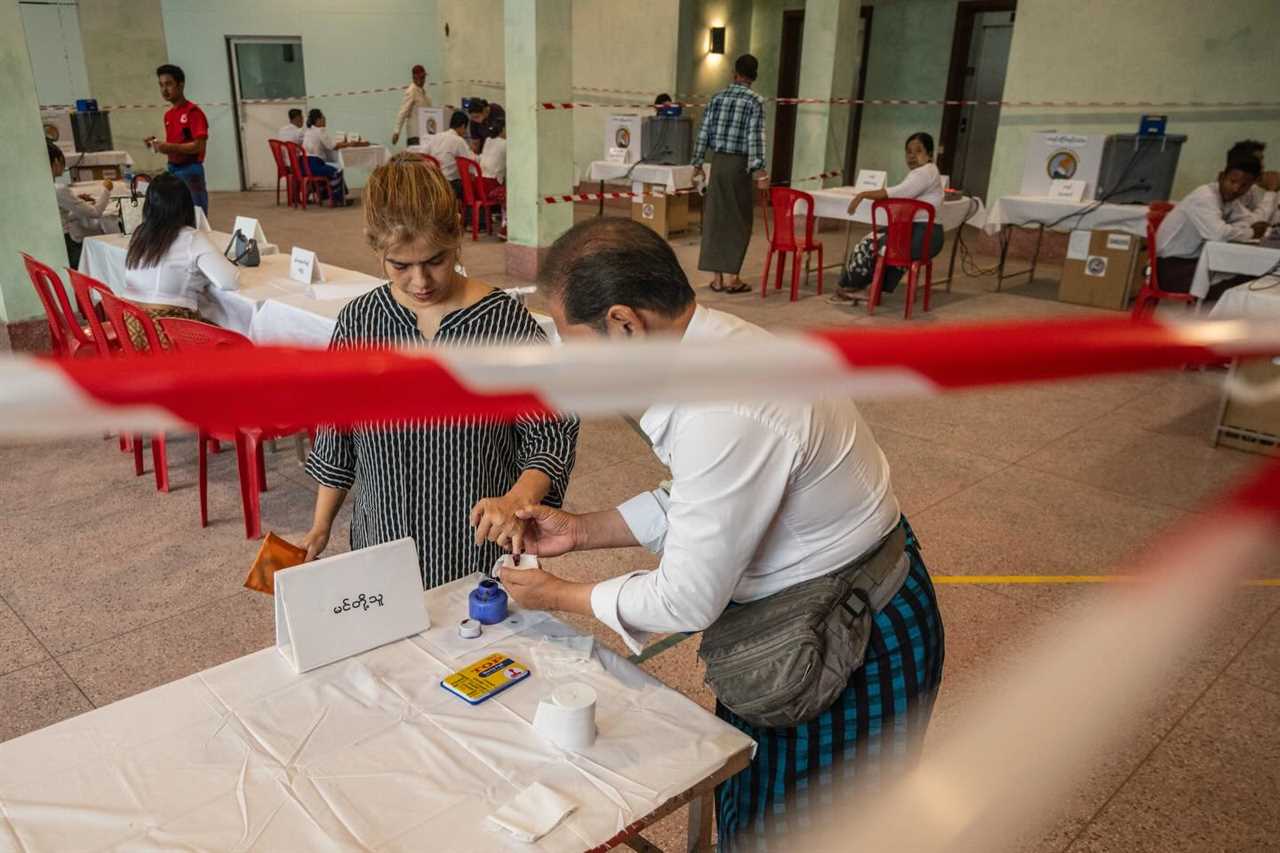 Voters participating in an election process, receiving ink marks at a polling station with social distancing measures in place.