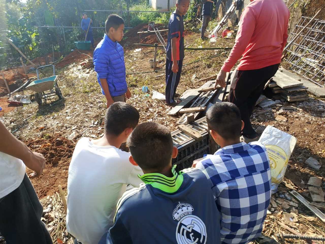 Group of young people engaged in outdoor construction work, with tools and materials visible in a rural setting.