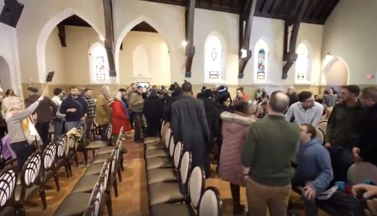 Crowd gathering in a church interior with arched ceilings and stained glass windows, showcasing a lively atmosphere during an event.