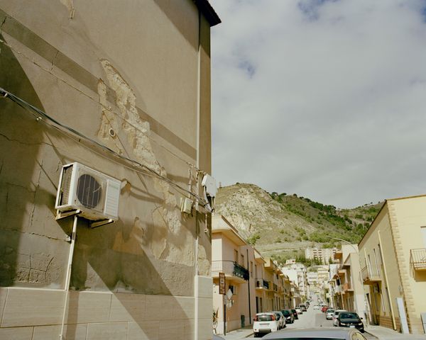 A street view with the family bakery behind looks toward the medieval hilltop commune of Erice. 