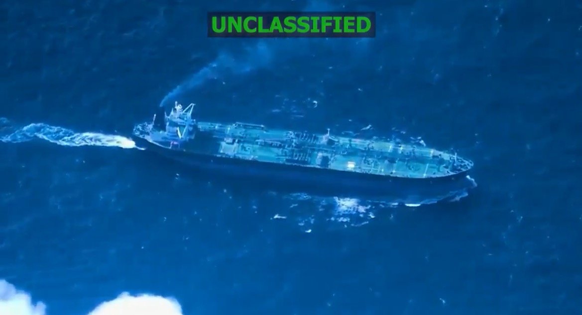 Aerial view of a large tanker ship navigating through deep blue ocean waters, emitting smoke from its exhaust.