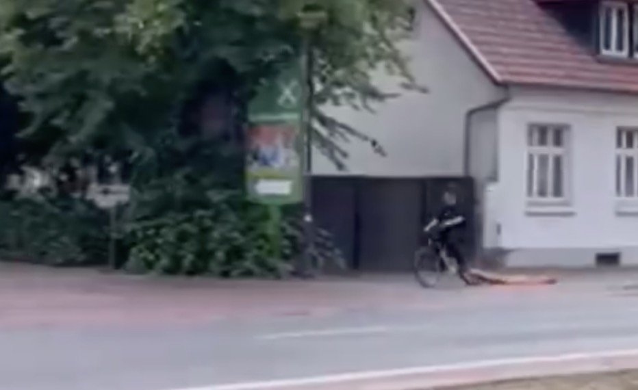 Person riding a bicycle on a city street near a building and a green sign.