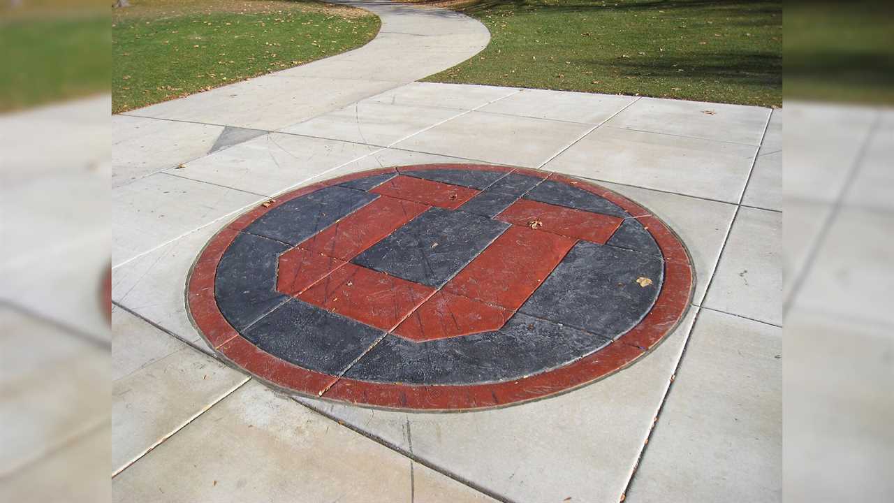University of Utah logo embedded in a circular stone design on a campus walkway surrounded by grass.