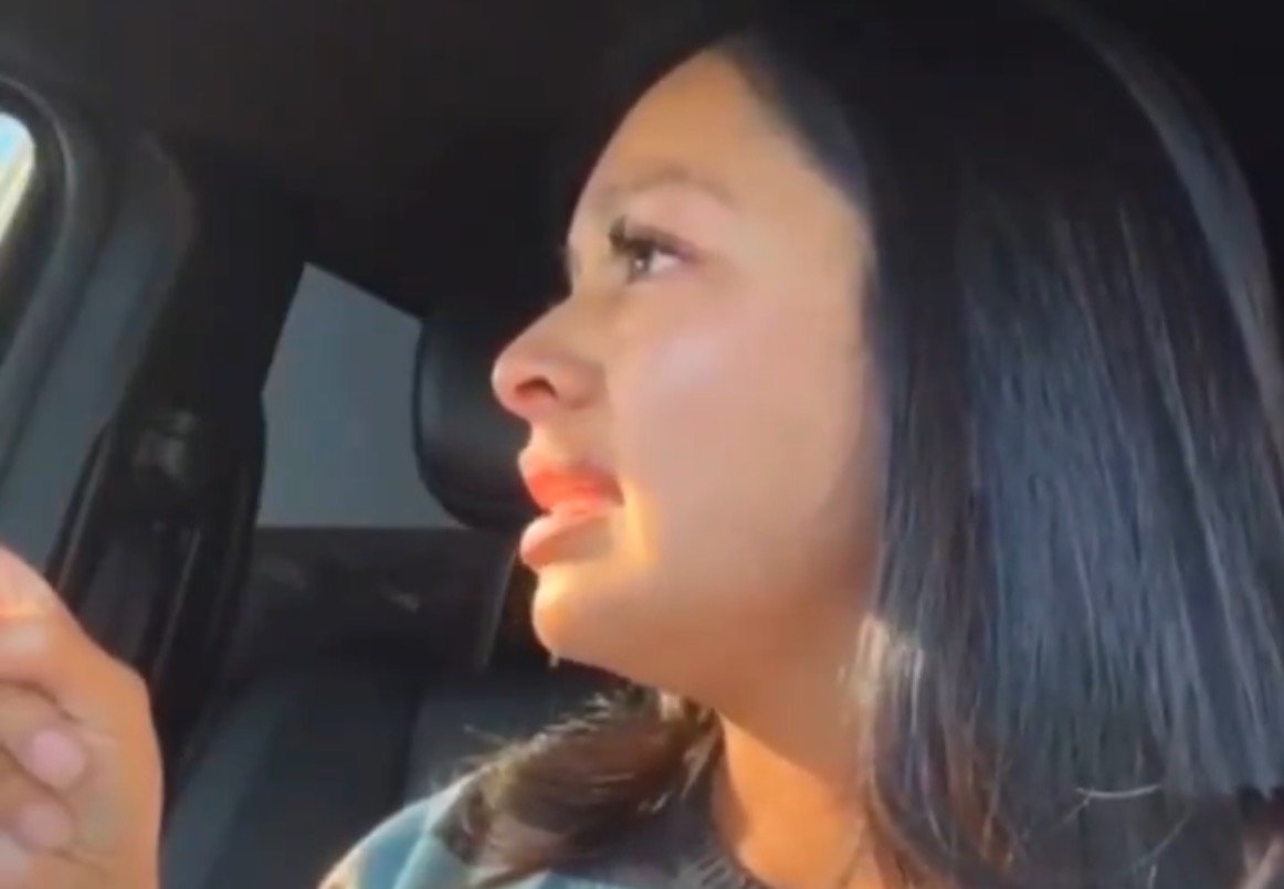 Woman in a car expressing emotions while speaking, with sunlight illuminating her face.