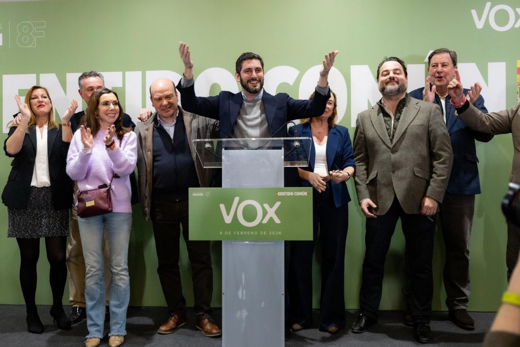 Vox political event featuring a group of supporters celebrating with raised hands and applause at a podium, promoting unity and community engagement.
