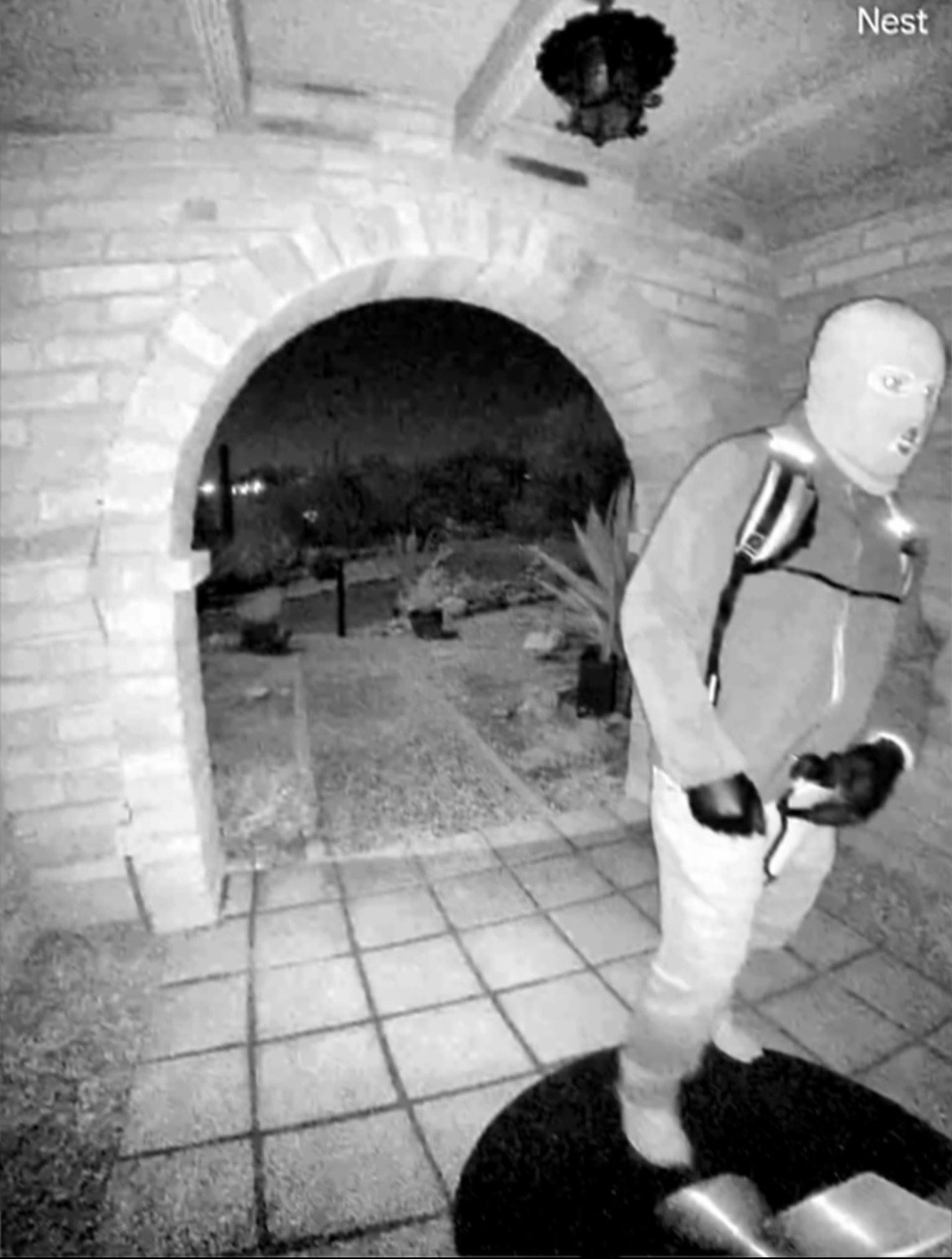 Intruder captured on a home security camera at night, wearing a mask and gloves, standing on a porch with a backpack.