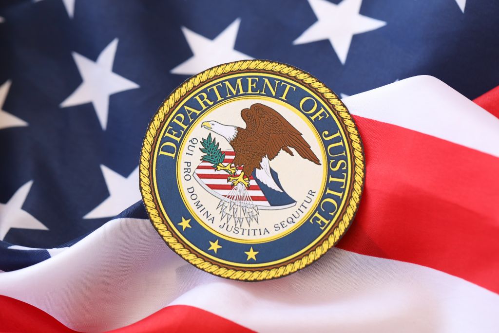 Seal of the U.S. Department of Justice resting on a backdrop of the American flag, symbolizing law and order.