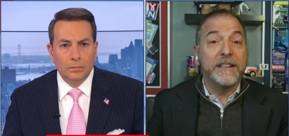 Two male news commentators discussing current events, with a city skyline visible in the background, showcasing a professional broadcast setting.
