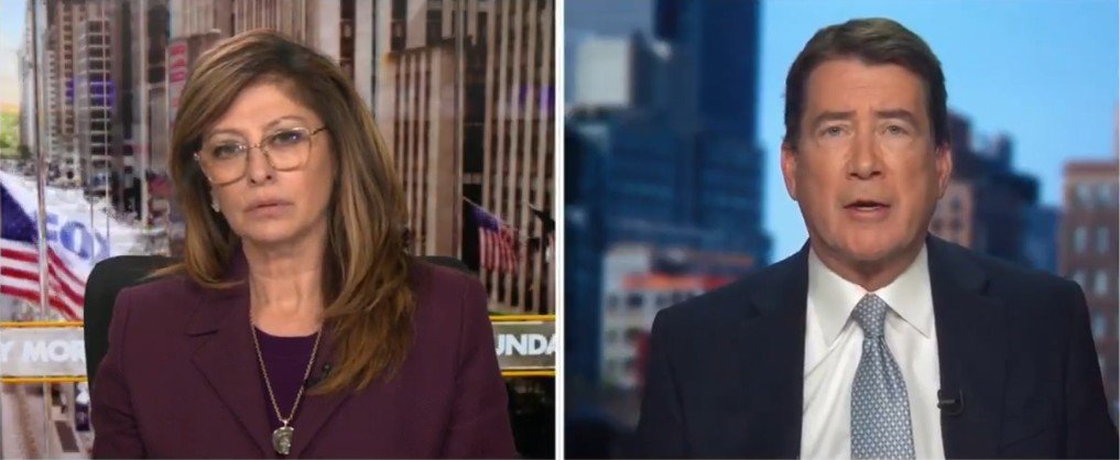 News anchors discussing current events with city skyline and American flags in the background.