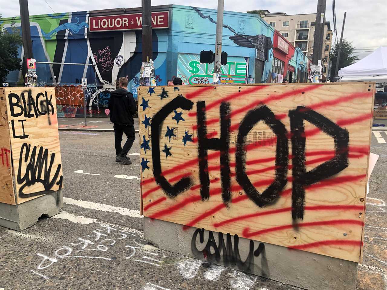 Wooden barriers with graffiti reading "CHOP" and "BLACK LIVES MATTER" in front of a liquor store, capturing a moment of community protest and activism.