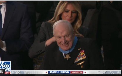Melania Trump smiles while adjusting the collar of a smiling veteran adorned with military medals at a formal event.