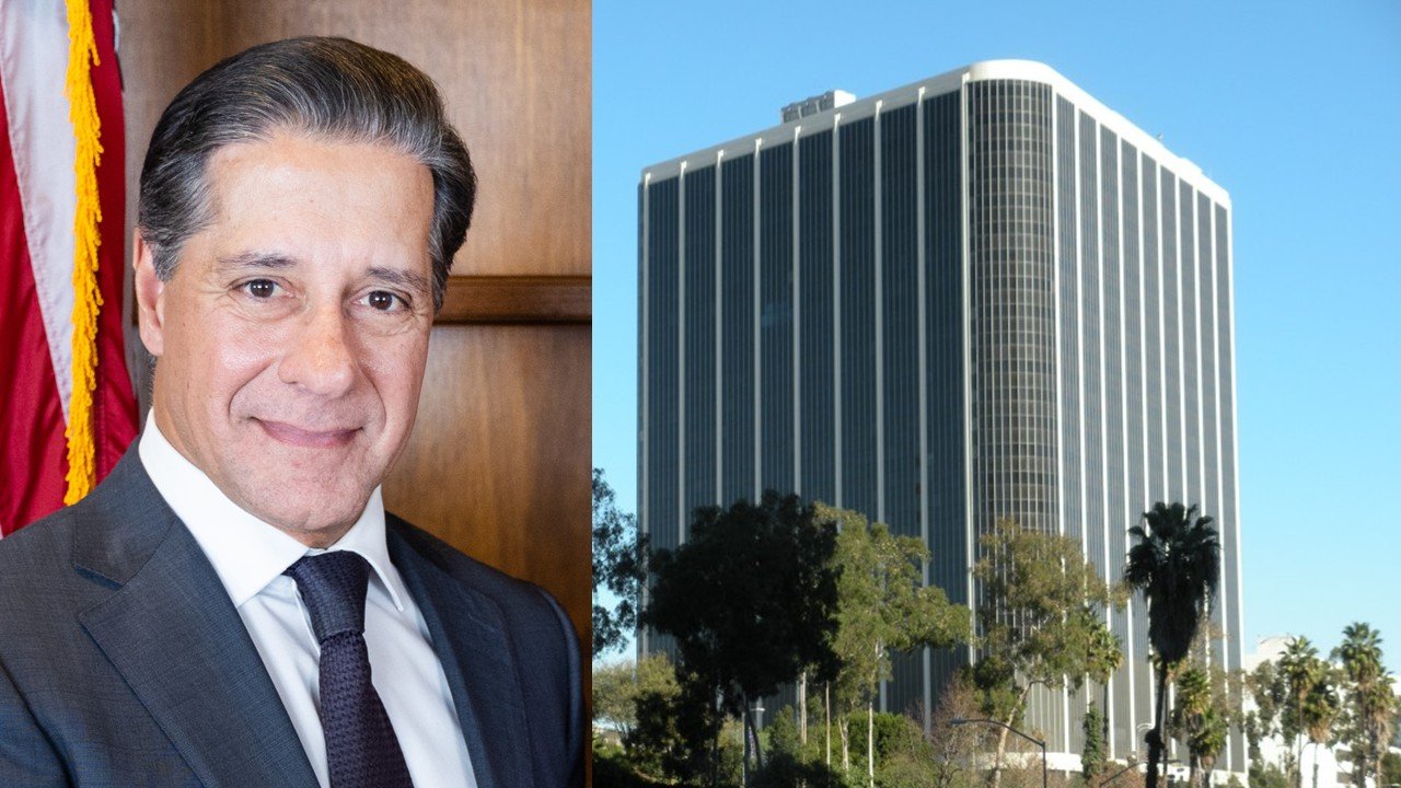Portrait of a professional man in a suit beside a modern office building surrounded by palm trees under a clear blue sky.