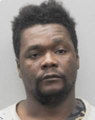 Mugshot of a man with short, curly hair and a neutral expression, wearing a patterned shirt, against a plain background.