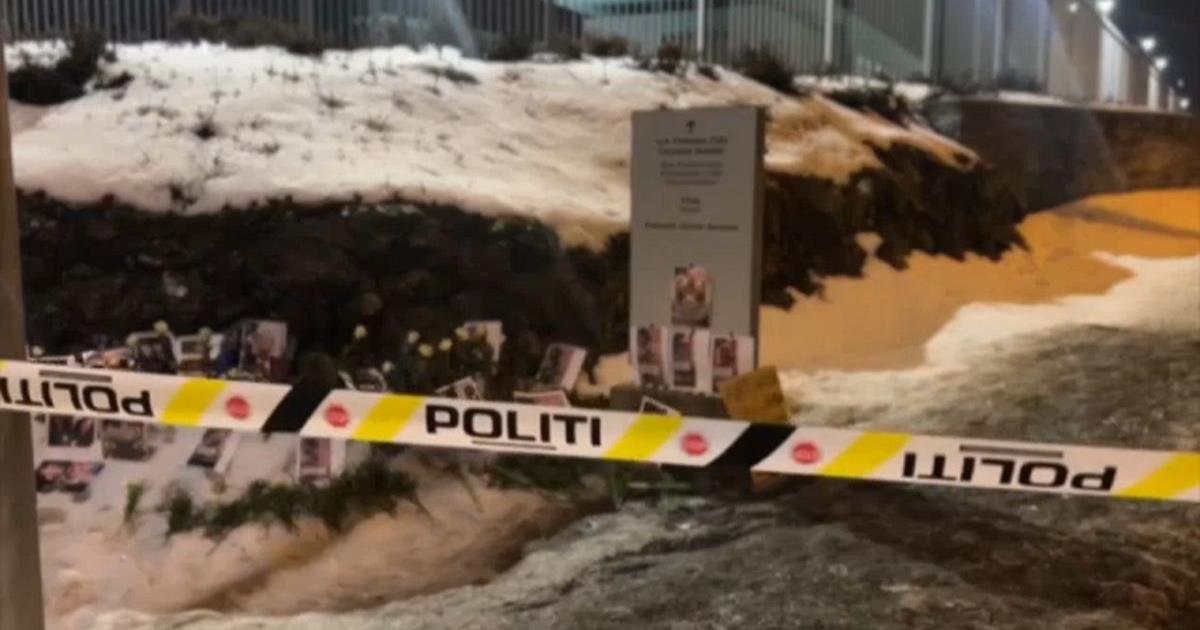Police tape surrounds a memorial site with flowers and photographs, set against a snowy landscape, indicating an ongoing investigation.