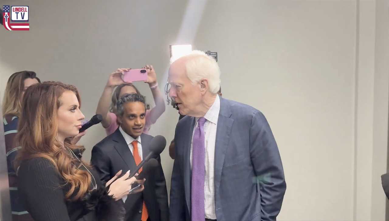 A reporter interviews a politician while another man observes, with onlookers capturing the moment on their phones in a professional setting.