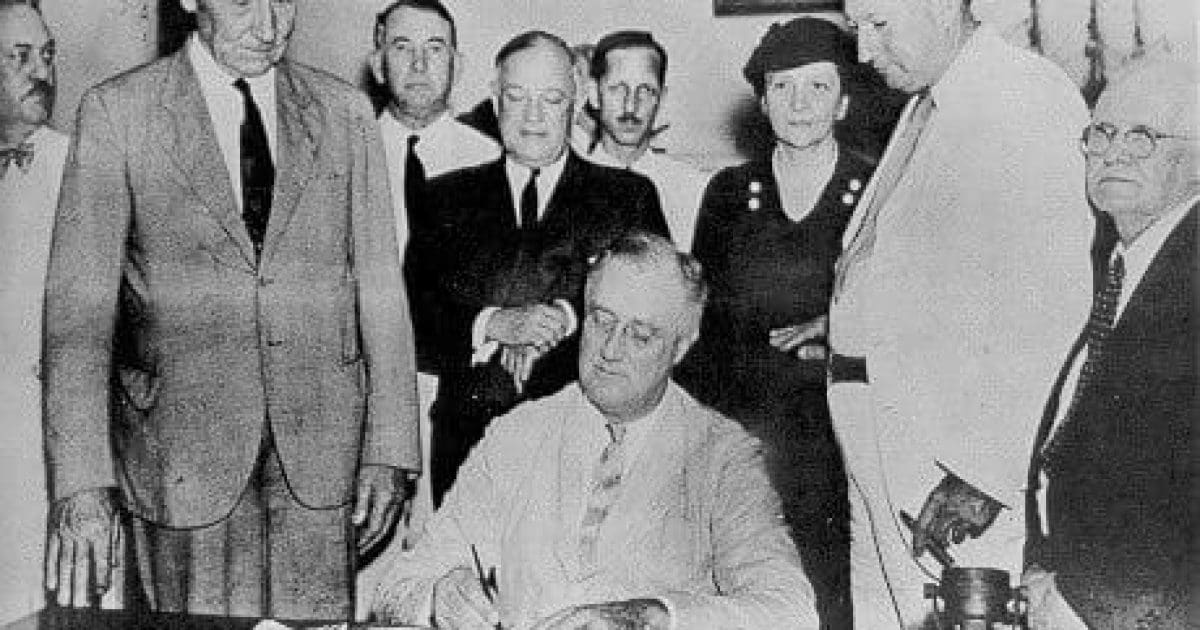 Historical photo of a group of officials surrounding a seated man signing a document, symbolizing a significant legislative action.