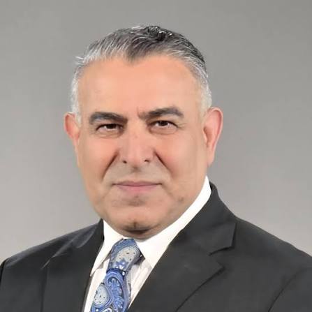 Professional portrait of a man in a black suit and patterned tie, showcasing a confident expression against a neutral background.
