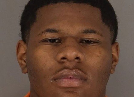 Mugshot of a young man wearing an orange prison uniform, displaying a serious expression against a neutral background.