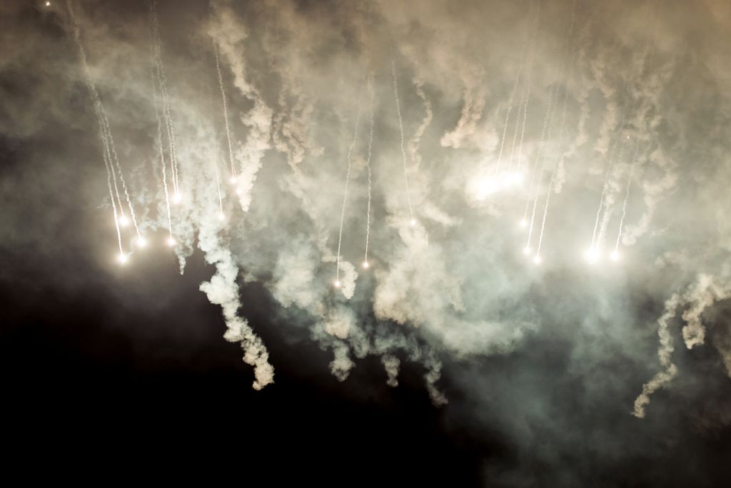 Colorful fireworks illuminate the night sky, surrounded by swirling smoke, creating a dramatic and festive atmosphere.
