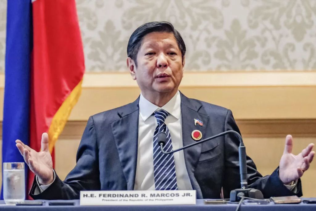 Ferdinand R. Marcos Jr., President of the Philippines, gestures during a formal discussion, with flags in the background.