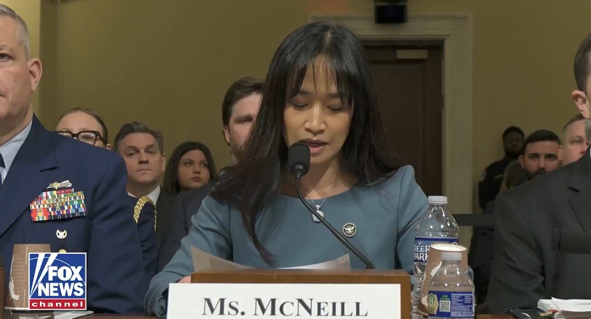 Ms. McNeill testifies at a congressional hearing, speaking into a microphone with military personnel and audience members present.