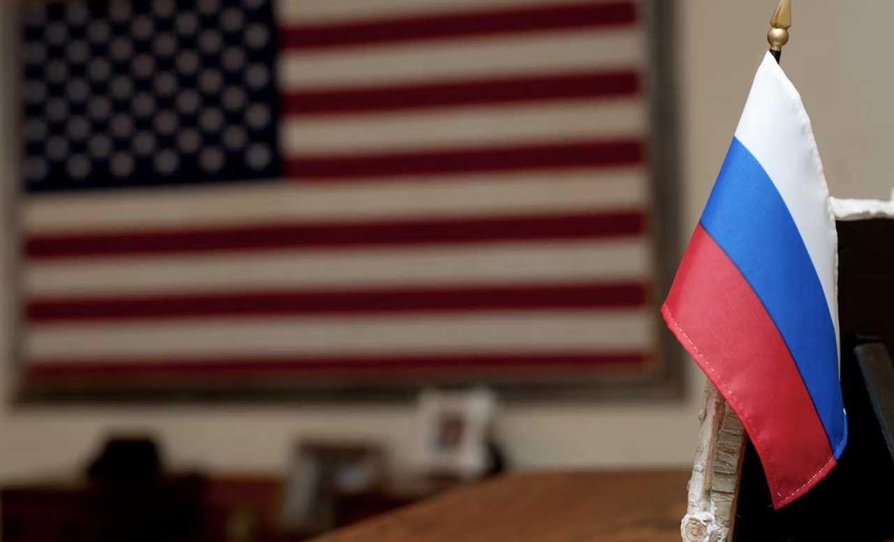 Close-up of a small Russian flag in front of a blurred American flag, symbolizing international relations and diplomacy between Russia and the United States.