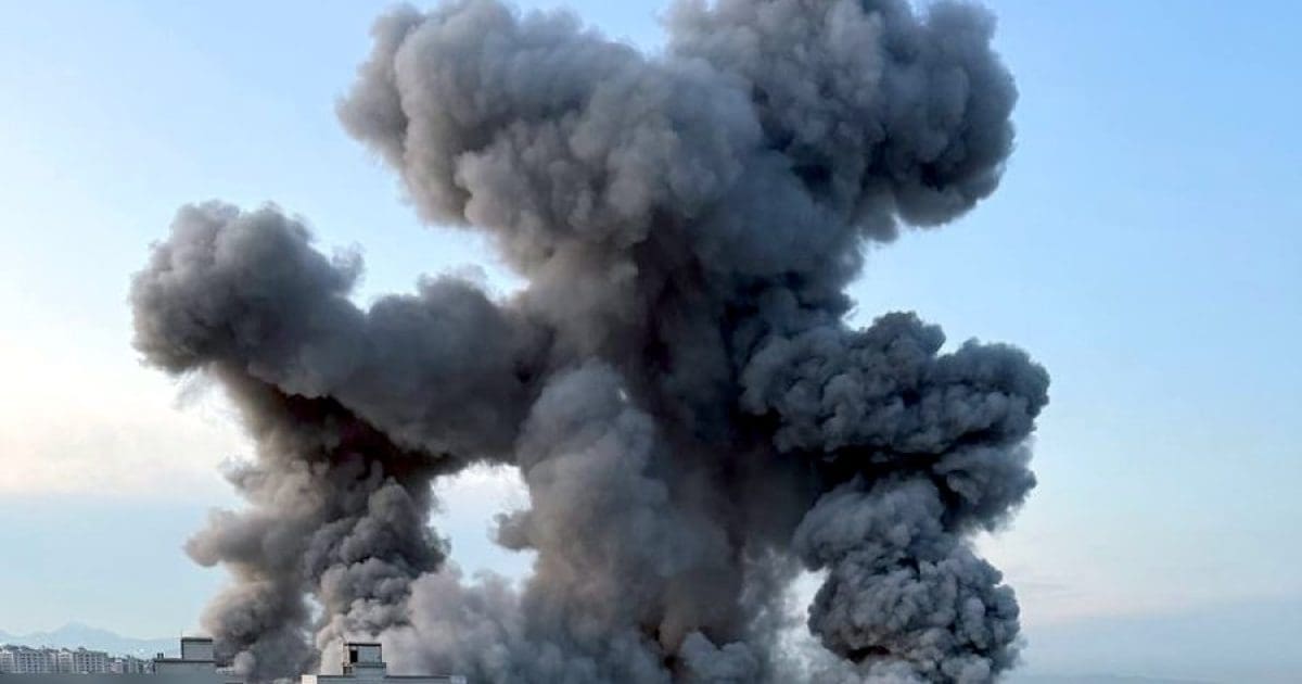 Thick black smoke billows into the sky from a large industrial fire, indicating a significant fire incident and potential environmental impact.