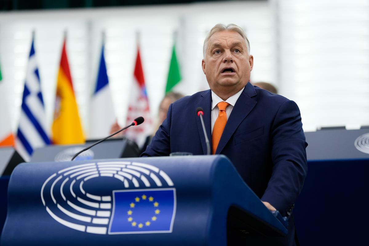 Hungarian Prime Minister Viktor Orbán delivers a speech at the European Parliament, with flags of EU member states in the background.