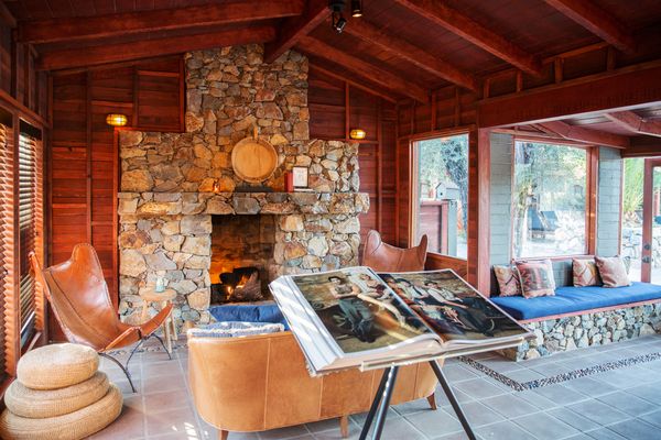 The barn-like reception area at Sparrows Lodge—which was built in 1952 by MGM actor Don Castle and his wife Zetta—retains its original stone fireplace and exposed timber beams, furnished with leather butterfly chairs and a built-in window seat.