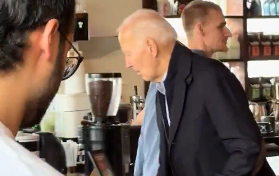 President Joe Biden visits a café, interacting with staff and patrons while exploring the coffee shop environment.