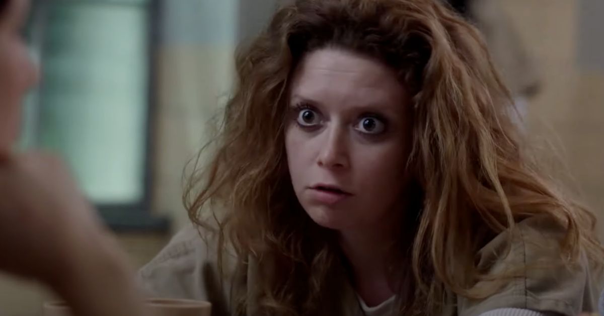 A woman with wild, curly hair sits at a table, intensely engaging in conversation in a prison setting.