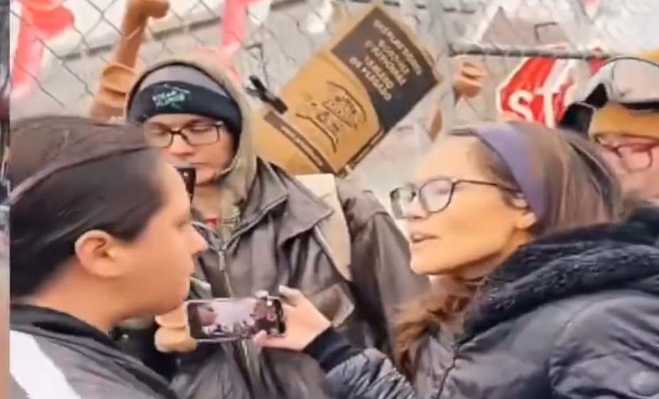 Two individuals engage in a heated discussion at a protest, surrounded by signs and onlookers, highlighting social activism and community engagement.