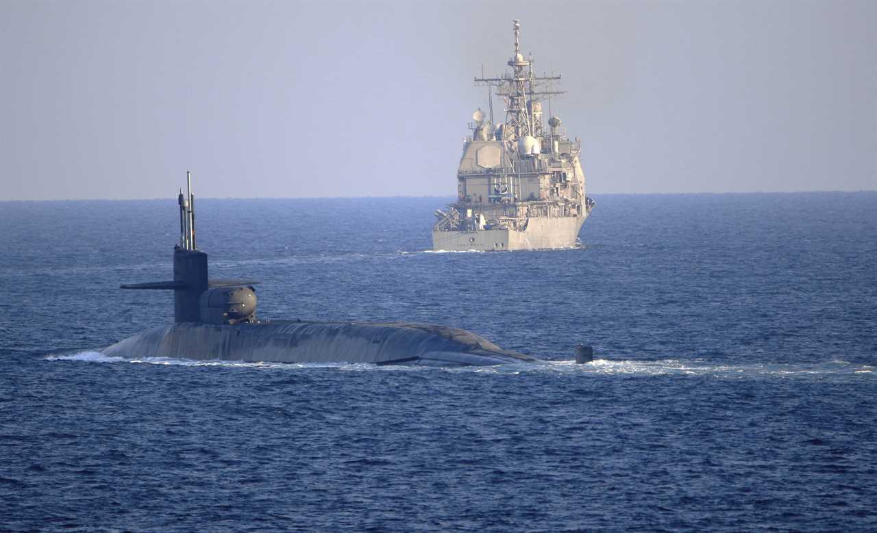 A submarine and a naval ship navigate through calm ocean waters, illustrating military maritime operations and naval collaboration.