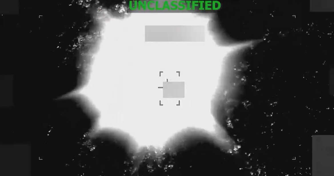 Aerial view of an explosion captured from a military drone, labeled as unclassified, highlighting the blast's intensity against a dark background.