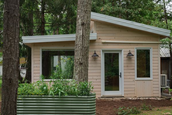The pine-clad guest cottage designed by Home by Tim + Chris in Kawartha Lakes, Ontario, Canada measures 260 square feet and is shaded by a grouping of old-growth trees.