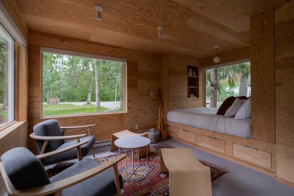 In the living area, the plywood walls, ceiling and sleeping nook with a queen bed and integrated storage reference the tree trunks that surround the structure. The upholstered armchairs, table, and stools are from Gus Modern; the flooring is Marmoleum by Forbo.