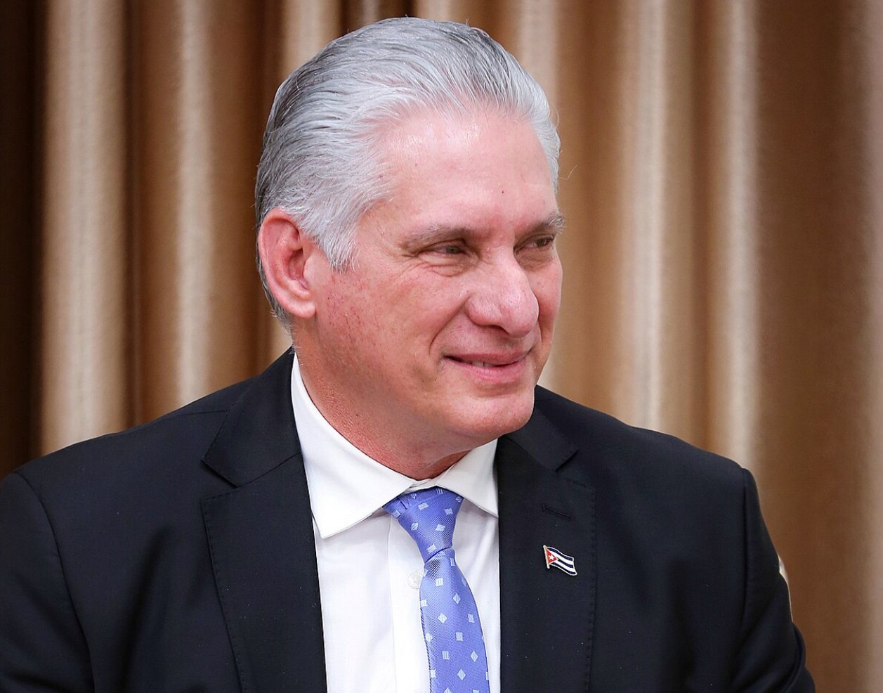 Cuban leader Miguel Díaz-Canel smiles during an official meeting, showcasing his formal attire and a Cuban flag pin on his suit.