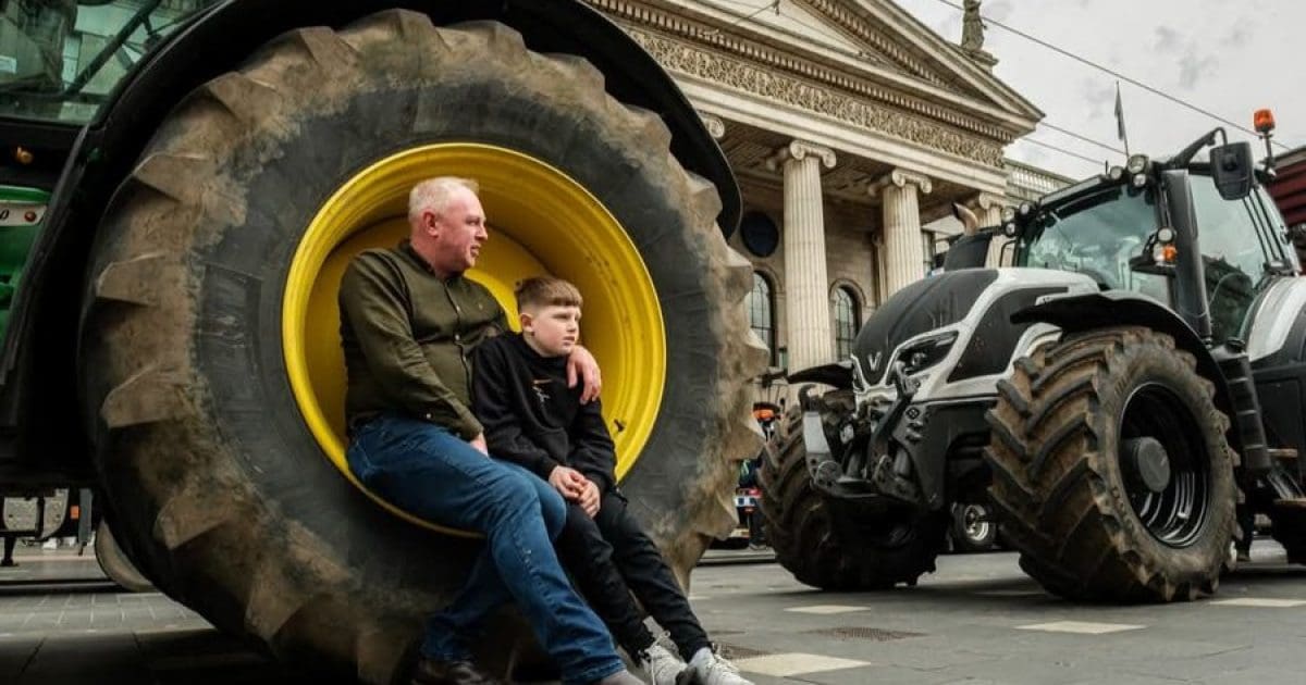 A man and a boy sit on a large tractor tire in front of a historic building, highlighting agricultural themes and community.