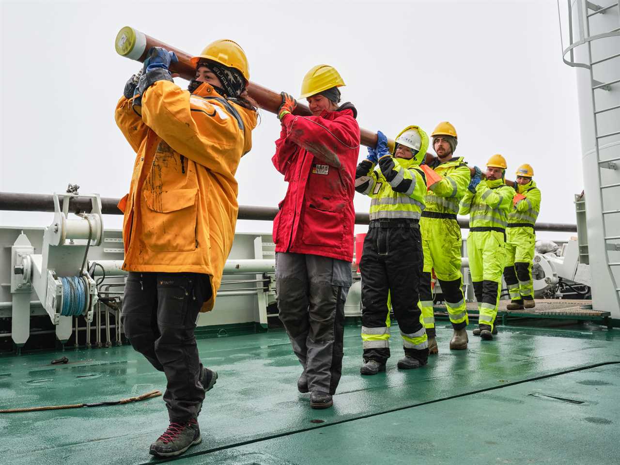 the crew in a line with the long pipe hoisted over their shoulder