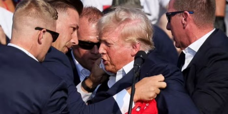 Donald Trump is surrounded by security personnel during a public event, emphasizing the heightened security measures in place.