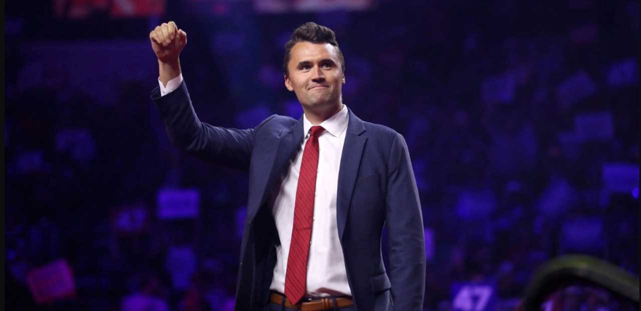 Man in a suit raising his fist in a crowd, expressing confidence and enthusiasm at a public event.