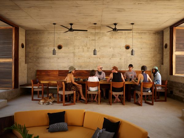 A communal gathering space at the center of the home includes a dining area, a kitchen, and a circular conversation pit upholstered in a mustard color that is carried through to the private rooms. 