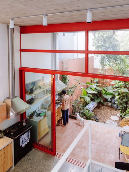 Separated by sliding doors with startling red frames, a pair of kitchens feature almost matching hoods for the indoor range and the outdoor grill. The polka-dot garden bench was designed by Estúdio Rôza with tile from Atelier Leopardi.