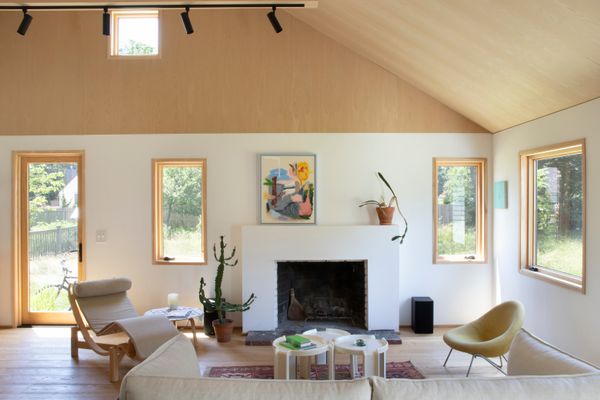 To make the interior feel more spacious, the architects opened the ceilings to create a double height space. They clad everything above eight feet, the original ceiling height, in plywood to maintain a human scale and the house’s original proportions. The sofa is from Hay, the Tokyo chaise lounge is from a now-closed Bellport vintage shop, the coffee tables are by Giotto Stoppino, produced by Kartell 1950s and 1960s, and the yellow chair, inspired by Pierre Paulin, was a find at Wright Auctions. Lisa painted the artwork on the mantel.