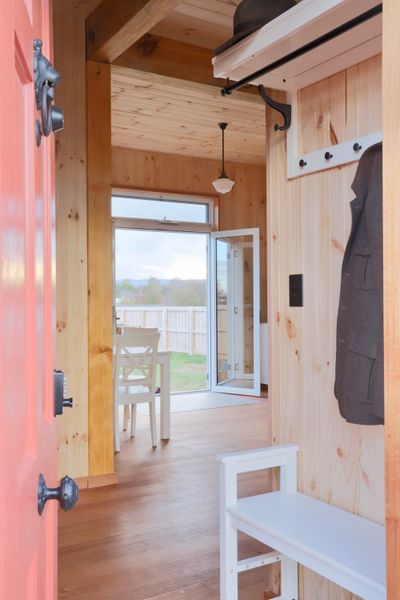 The bright red front door opens to a small entry hall with storage and seating. This leads directly to the open-plan living, dining, and kitchen space. The furniture throughout is primarily from affordable Australian retailer Early Settler.